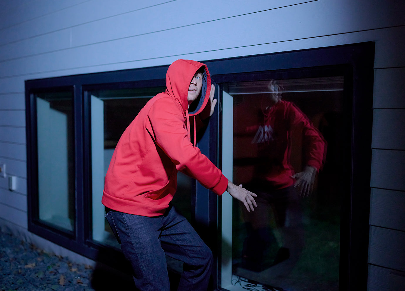 A burglar trying to break into a home with the Arlo Essential 3rd Gen XL camera shining a light on the burglar