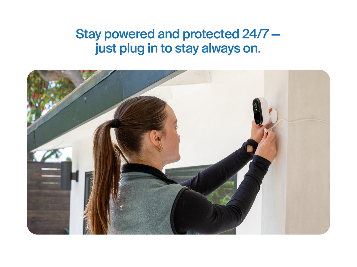 A woman plugging in the Arlo Essential Plug-in camera on the side of a house