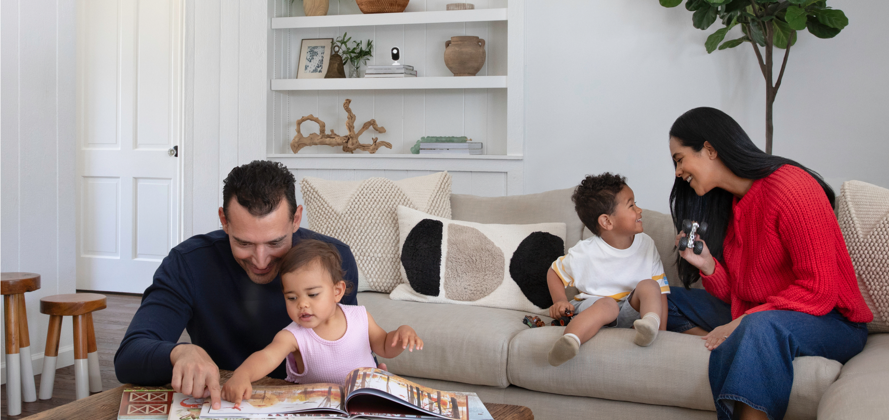 A family reading a book and playing on a couch with the Arlo Essential 3rd Gen Indoor camera on a book shelf