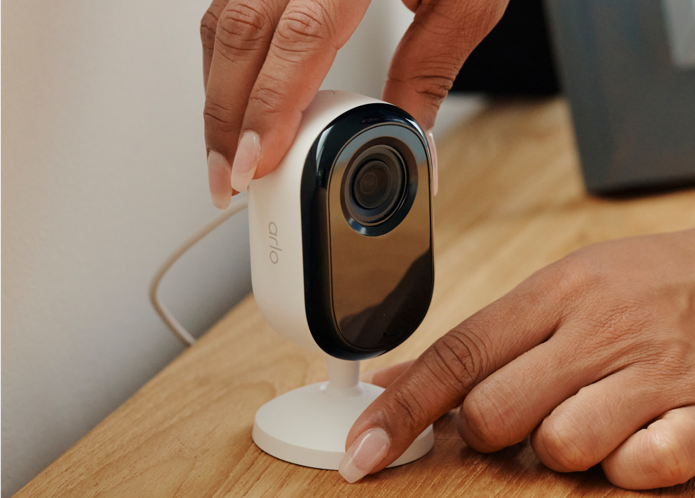 A person setting the Arlo Essential 3rd Gen Indoor camera on top of a wooden table