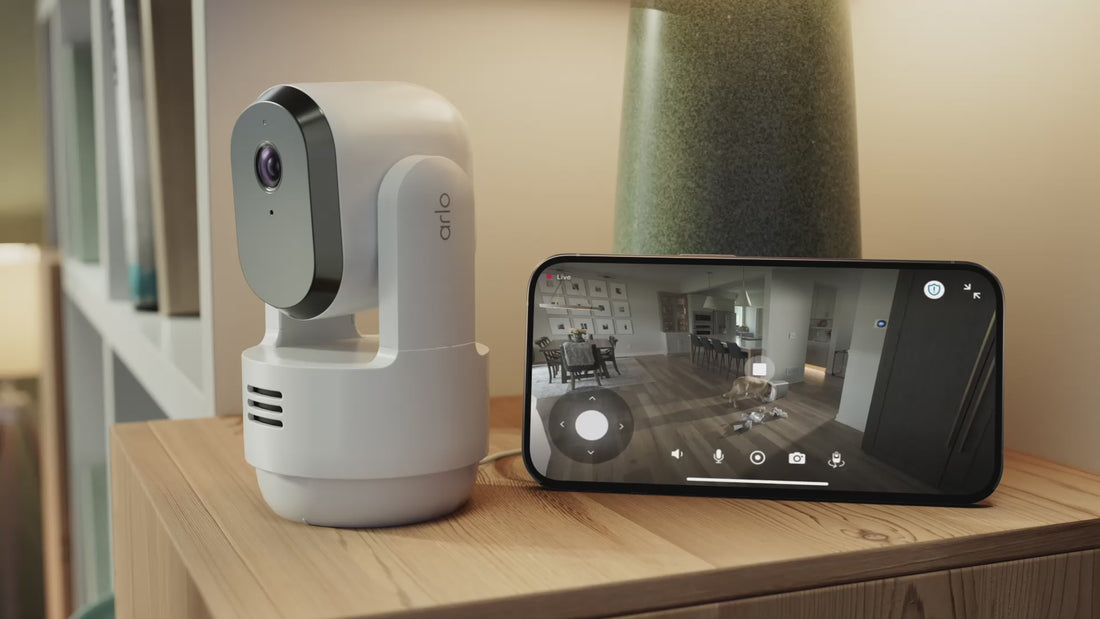 Arlo Essential 3rd Gen Pan Tilt Indoor camera next to a phone showing a dog eating garage out of a trash can on the phone screen